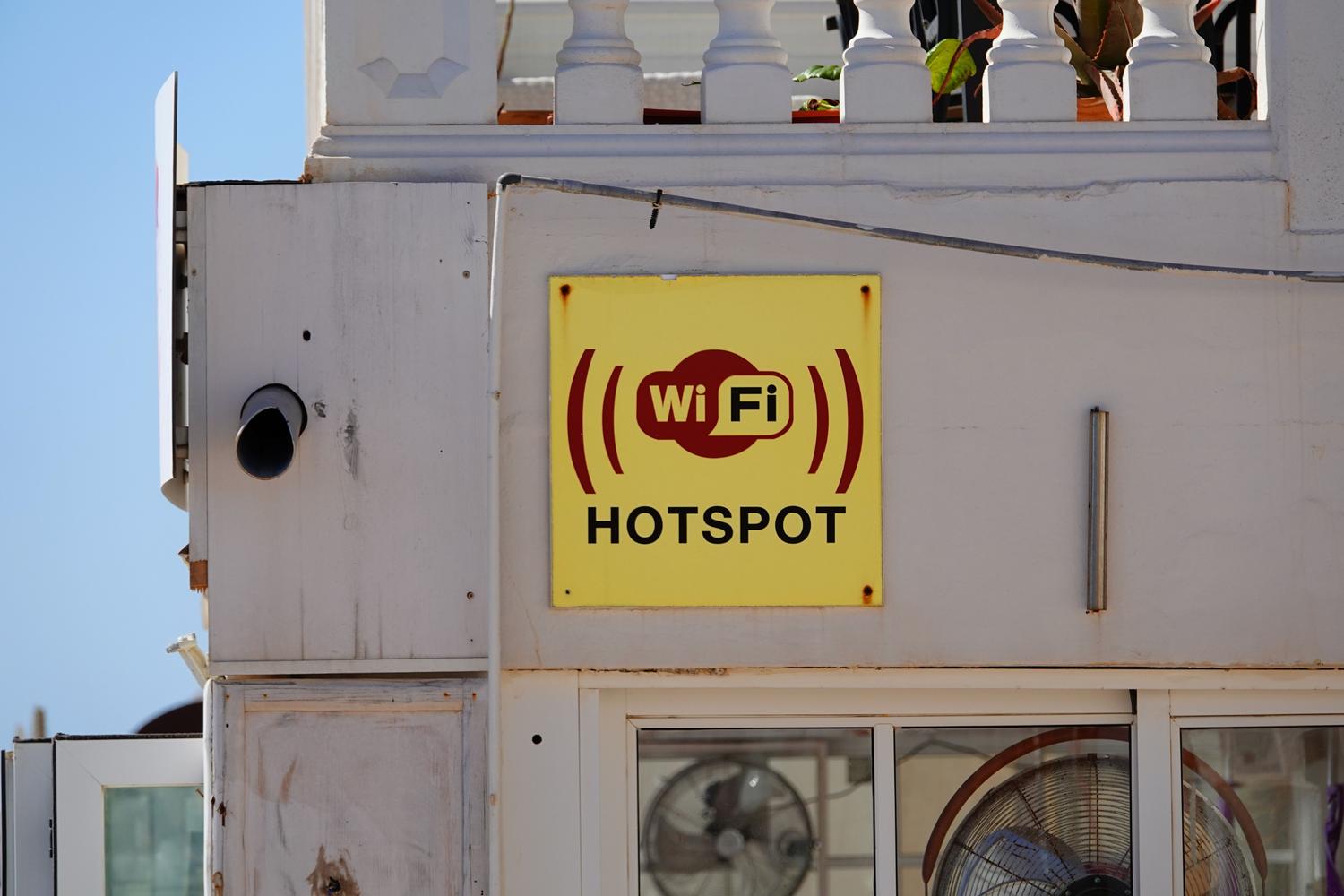 Cartel amarillo de punto de acceso WiFi en una fachada, utilizado para contrastar la inseguridad de las redes públicas frente a un MiFi privado.