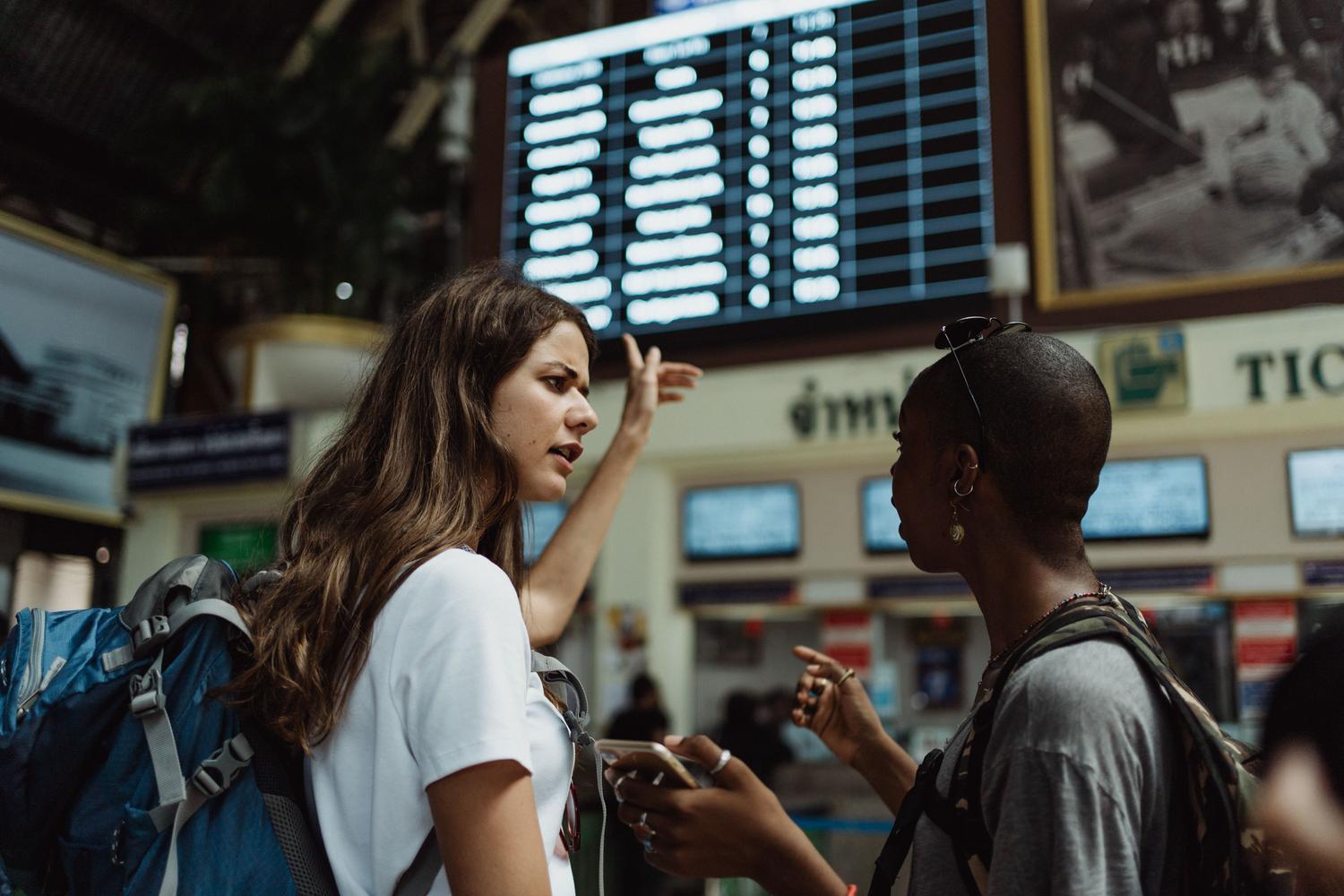 Dos viajeras interactuando en un aeropuerto internacional, simbolizando la comunicación global.