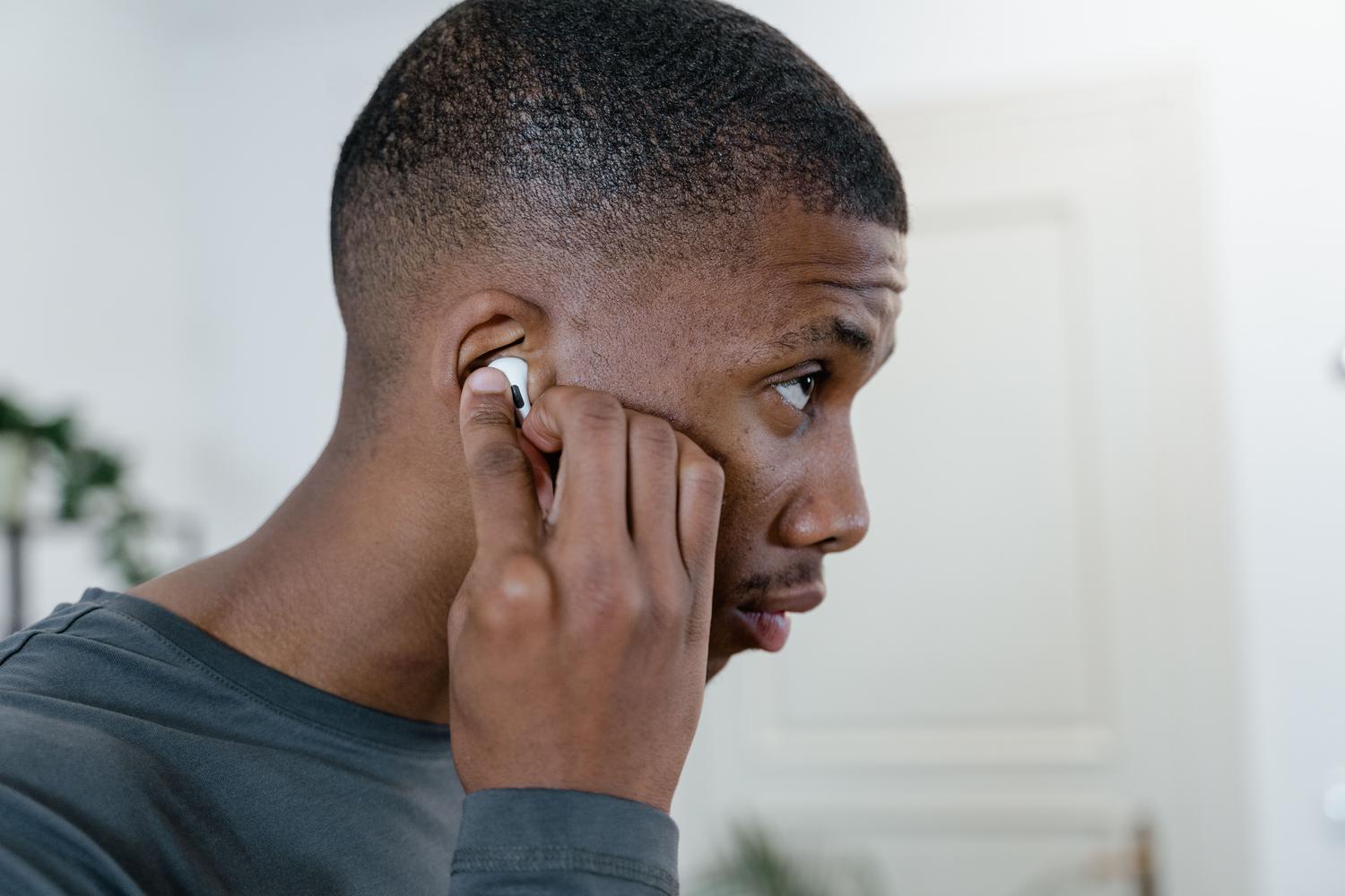 Hombre joven ajustando sus auriculares inalámbricos, destacando el estilo de vida moderno y conectado.