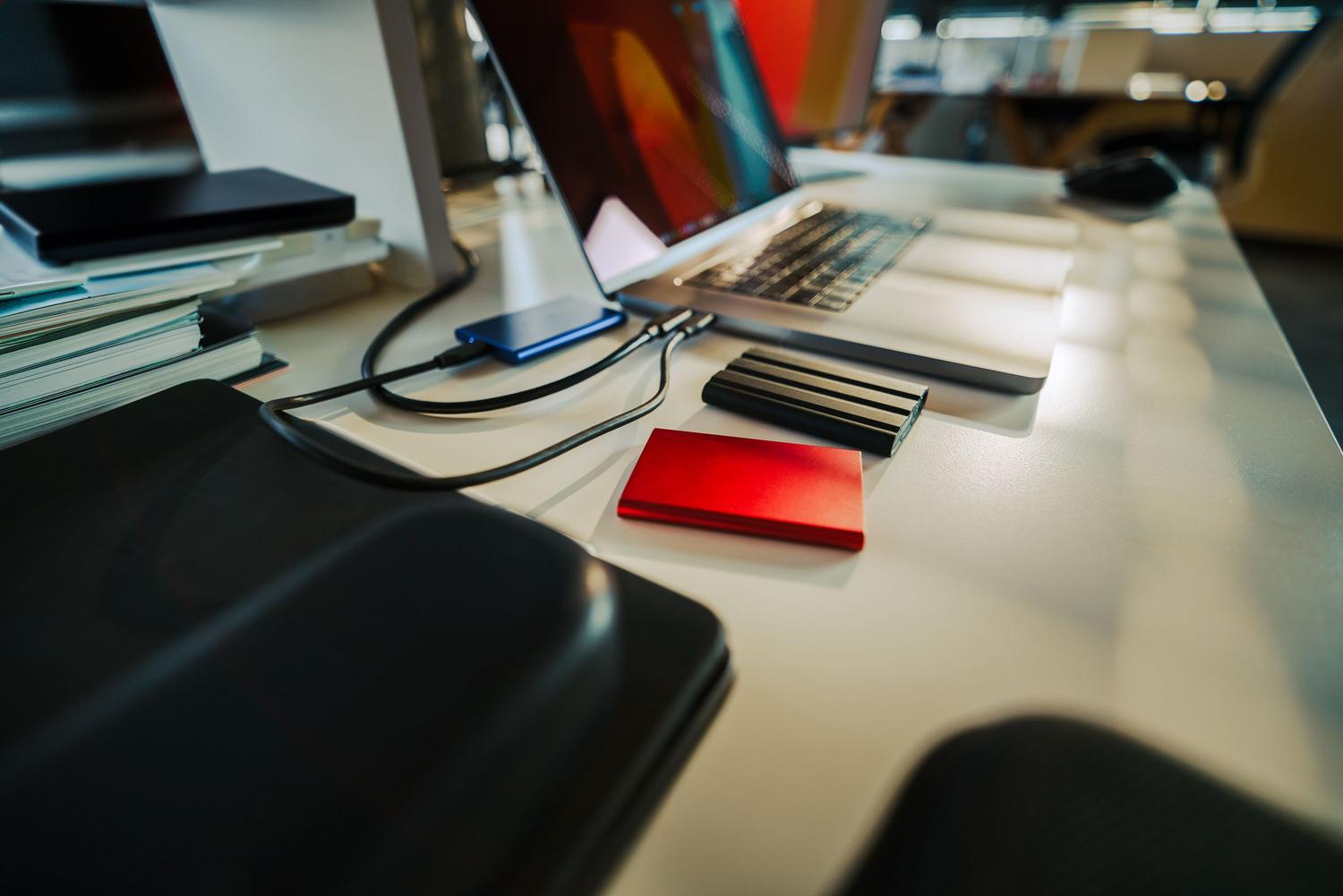 Escritorio de oficina organizado con un portátil y varios discos duros externos para copias de seguridad.