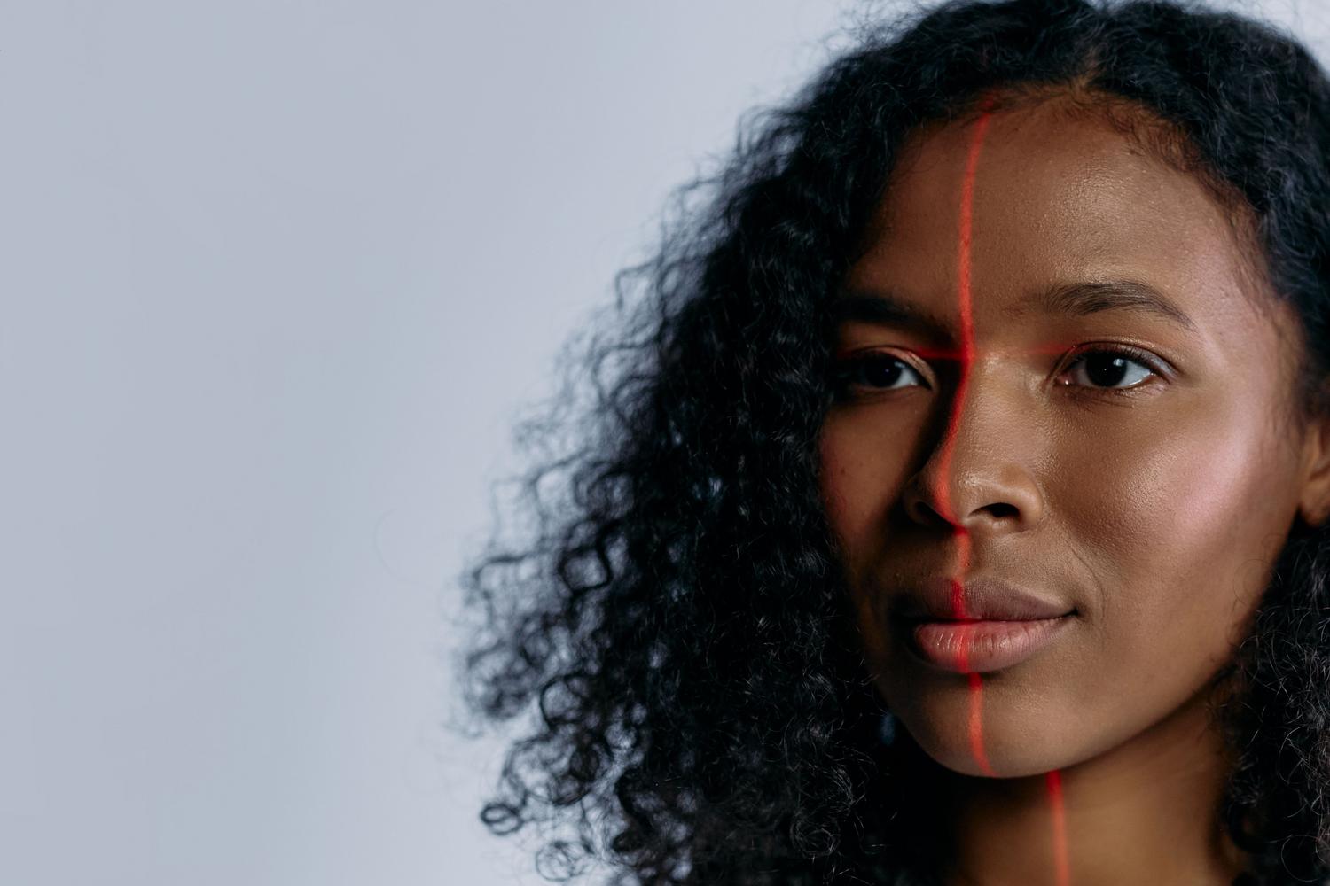 Primer plano de una mujer siendo escaneada con un láser rojo facial, ilustrando la tecnología de detección y análisis de rostros por IA.
