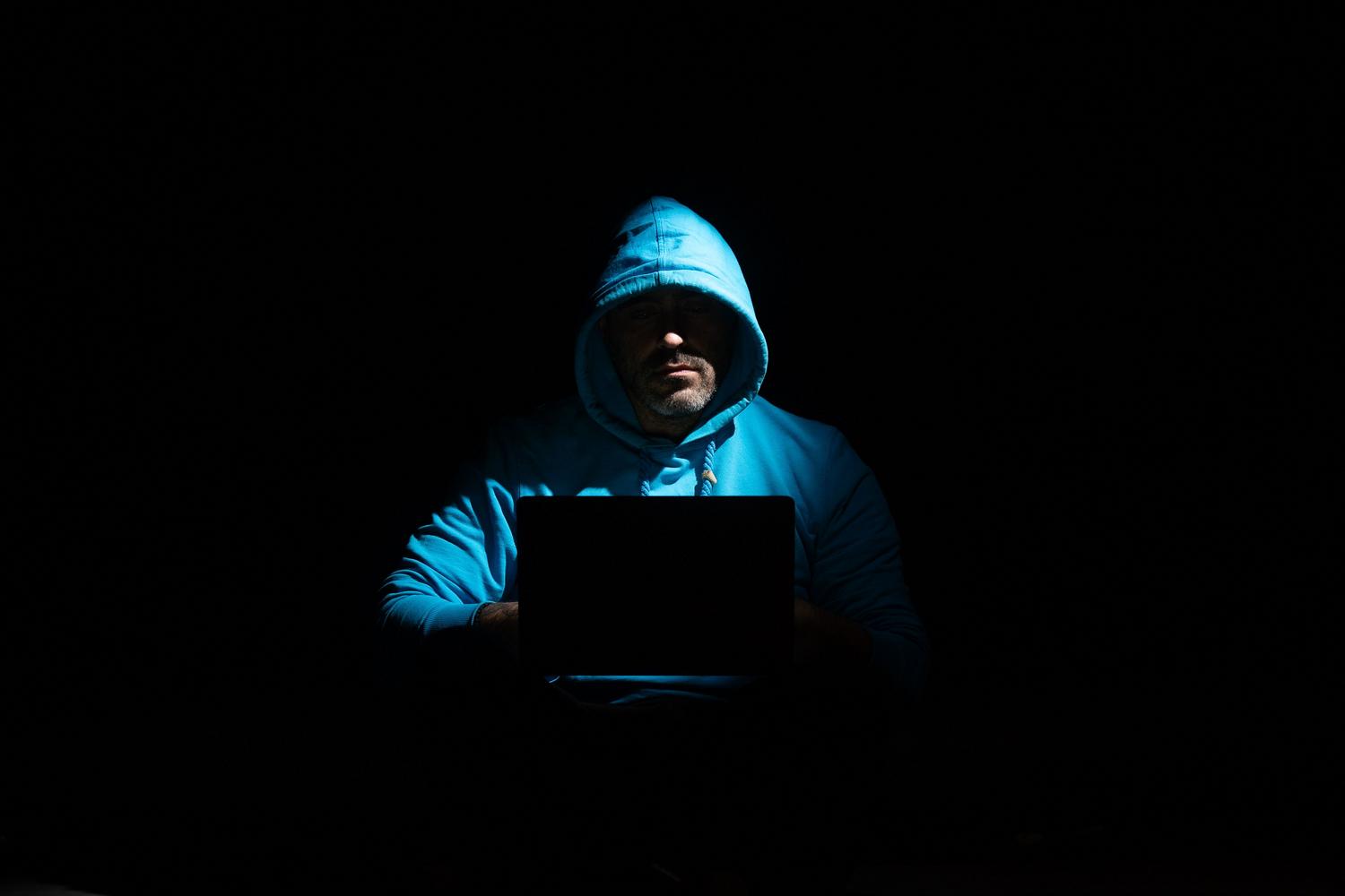 Persona encapuchada usando un portátil en la oscuridad, ilustrando los riesgos de seguridad y el misterio de la navegación anónima.