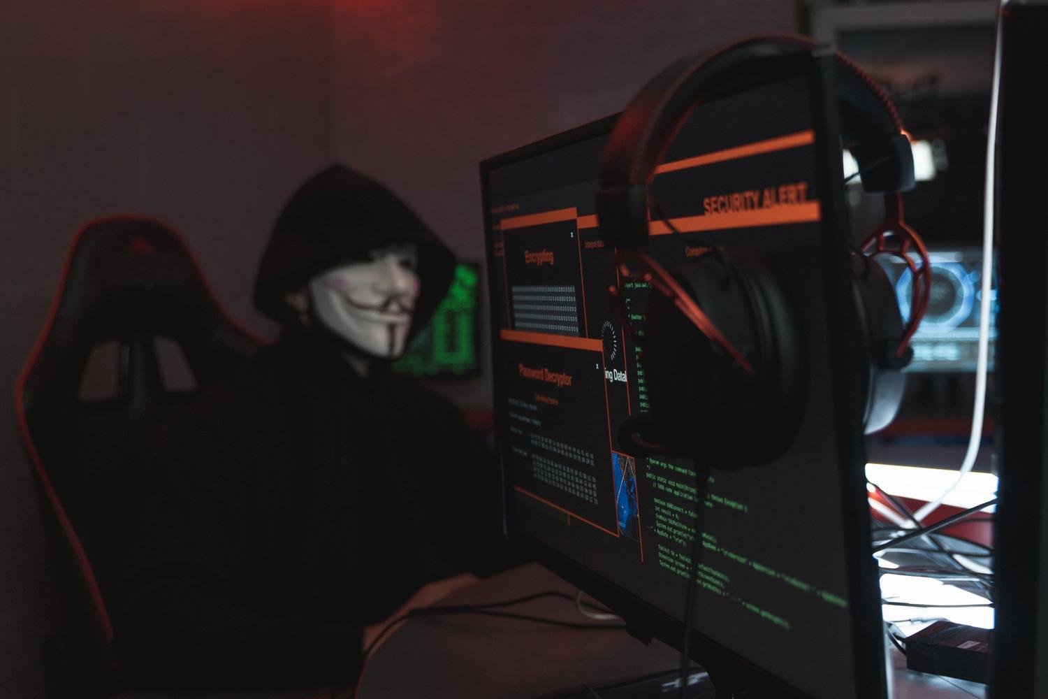Persona con máscara de Guy Fawkes frente a un ordenador, representando el anonimato y la cultura característica de la Dark Web.