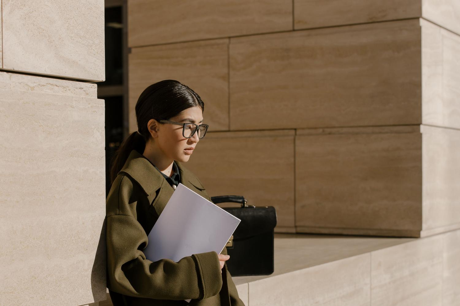 Mujer profesional con gafas y carpeta en un entorno urbano, ilustrando la importancia de una imagen profesional coherente.