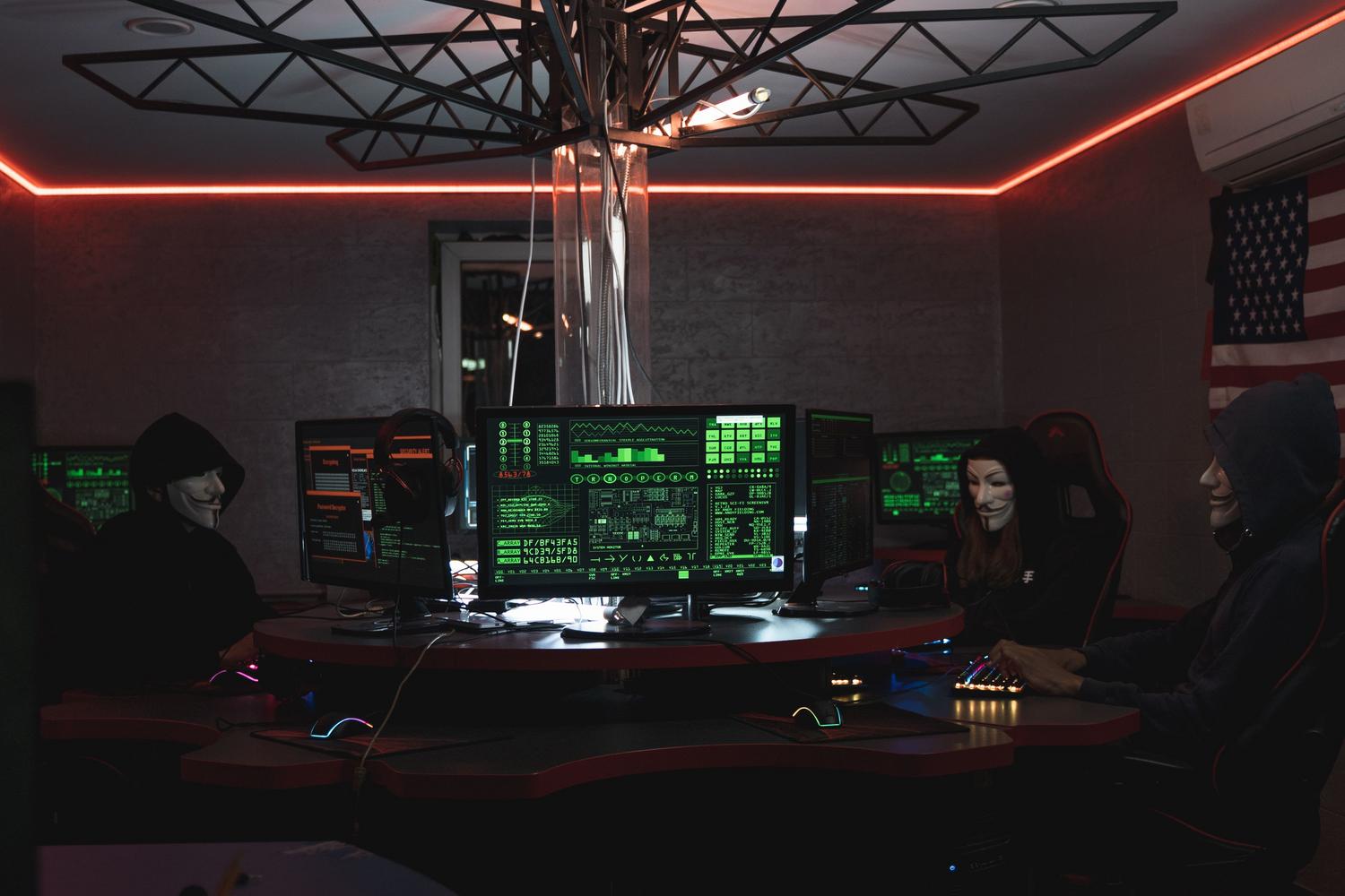 Grupo de atacantes informáticos con máscaras trabajando en un entorno oscuro, ilustrando las amenazas comunes como el malware y el hacking.