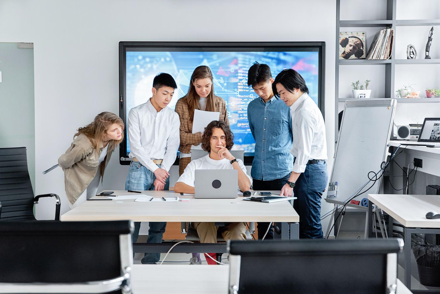 Equipo de trabajo diverso colaborando en tiempo real con un ordenador portátil en una oficina moderna.