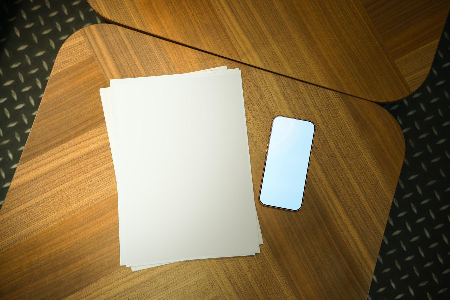 Vista cenital de un smartphone y hojas de papel sobre una mesa de madera, representando la digitalización de documentos