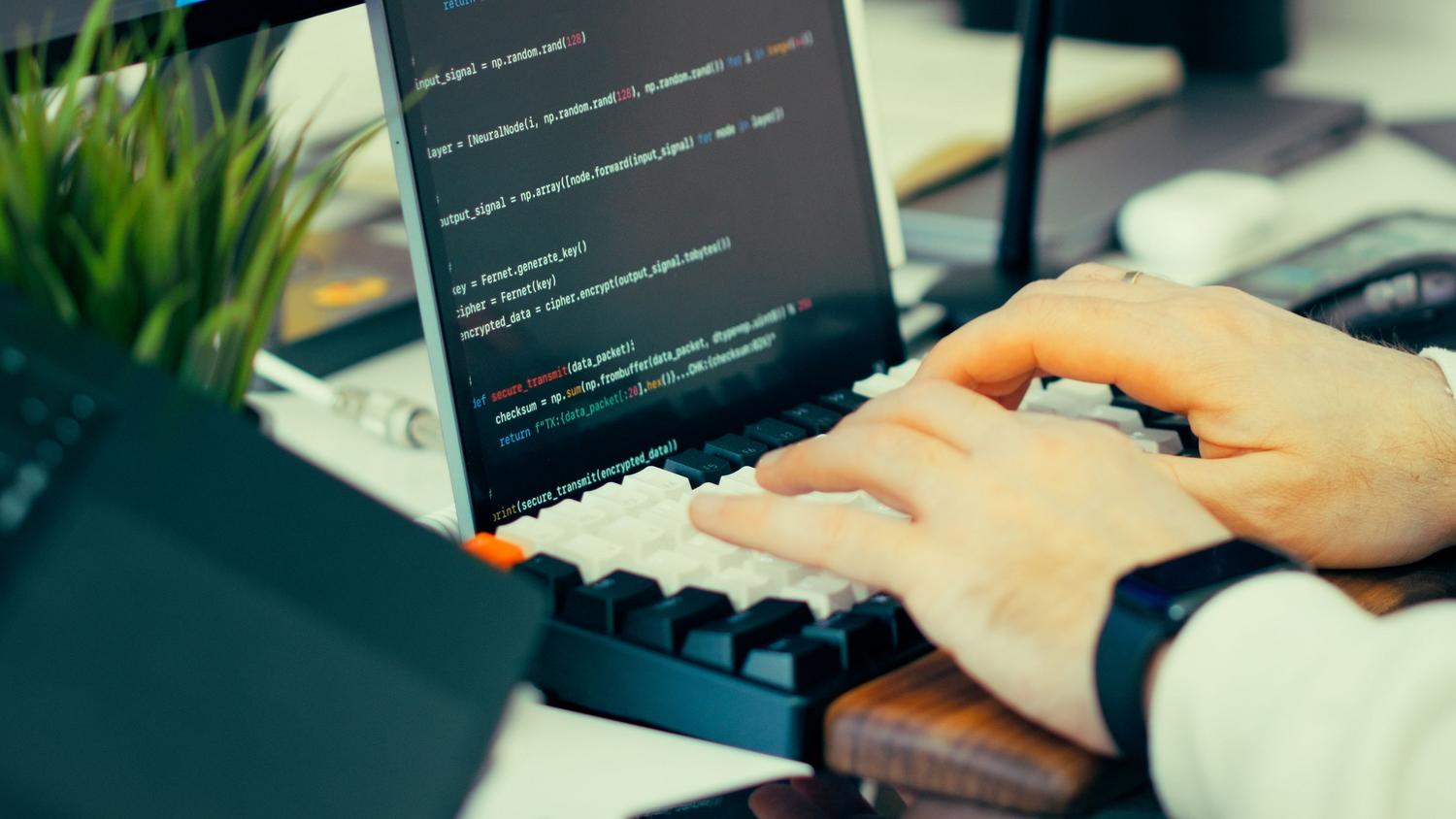 Primer plano de un desarrollador escribiendo código en un teclado con pantalla de scripts