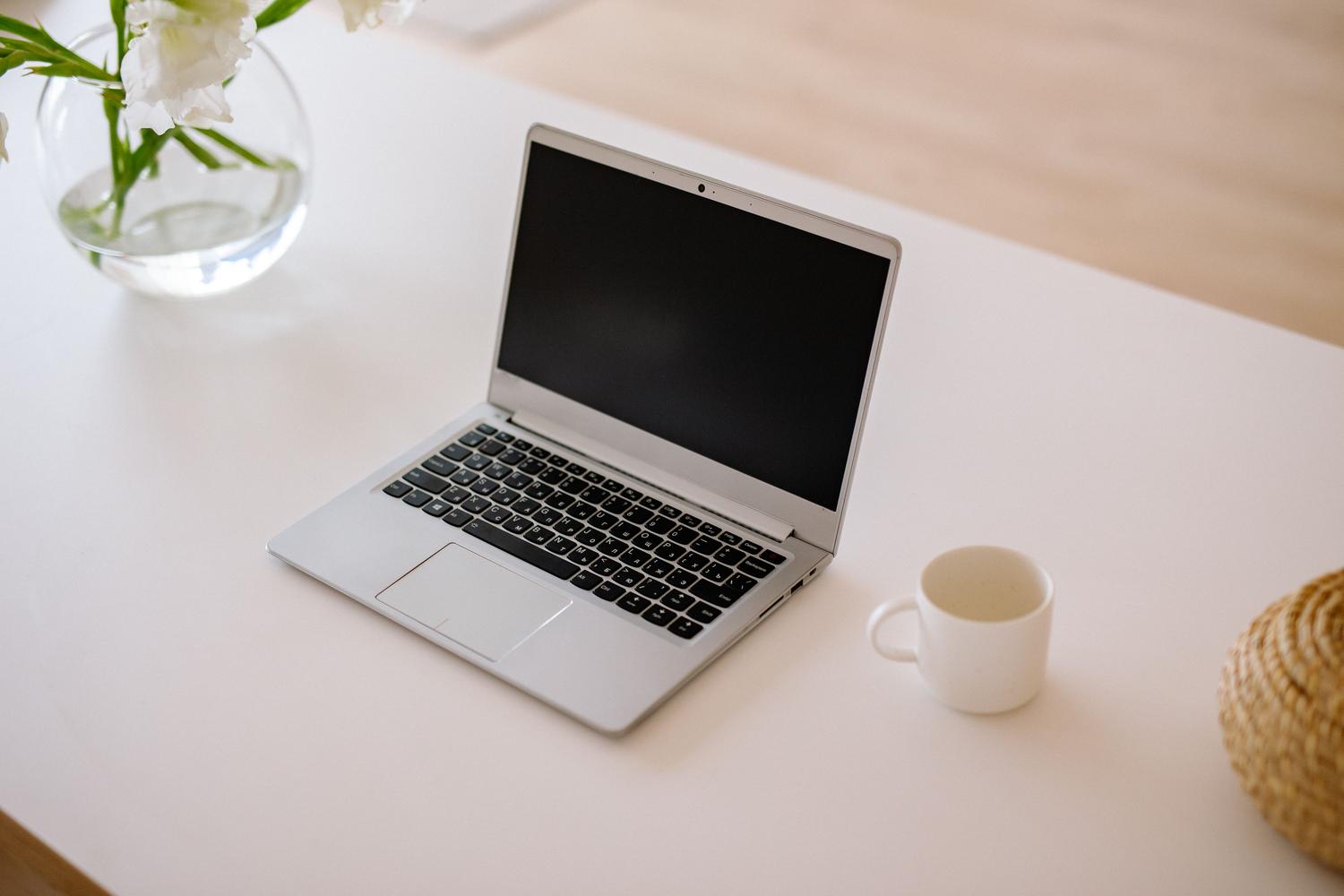 Espacio de trabajo minimalista con un portátil abierto y una taza de café sobre una mesa blanca