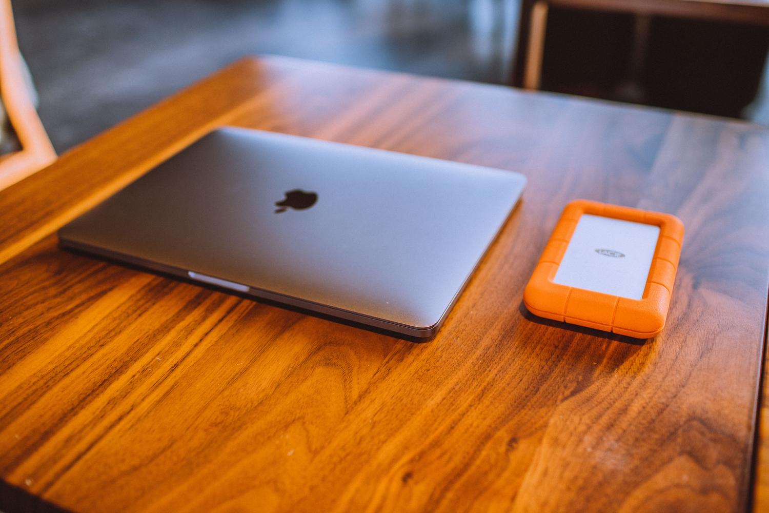 MacBook y disco duro externo robusto sobre una mesa de madera, ideal para representar el sistema de archivos APFS y copias de seguridad.
