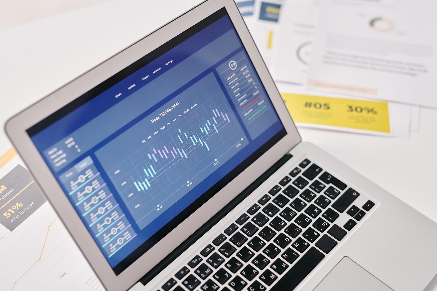 Laptop con panel de análisis de datos y documentos impresos, ilustrando la gestión de archivos y datos profesionales.