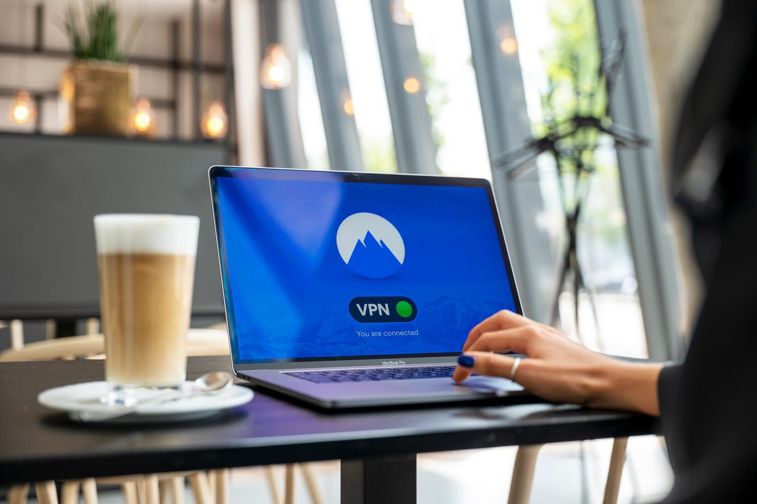 Persona utilizando un portátil en una cafetería con una conexión VPN activa para asegurar su navegación en Wi-Fi público.