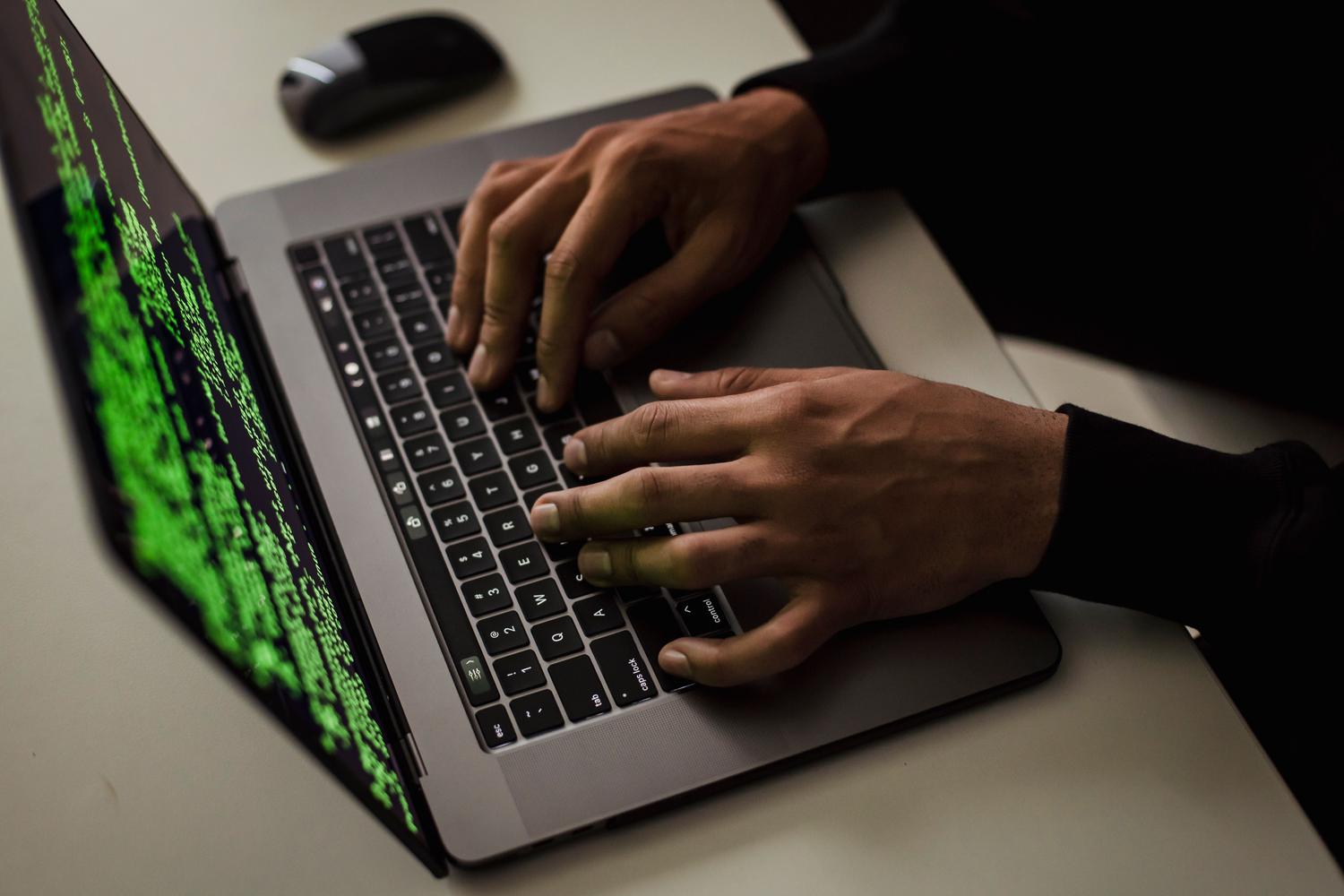 Imagen conceptual de un ciberdelincuente operando un ordenador con códigos en pantalla, representando la amenaza del malware.
