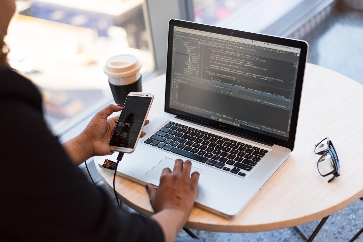 Desarrollador utilizando un portátil y un smartphone simultáneamente, destacando el soporte multiplataforma de Firebase.