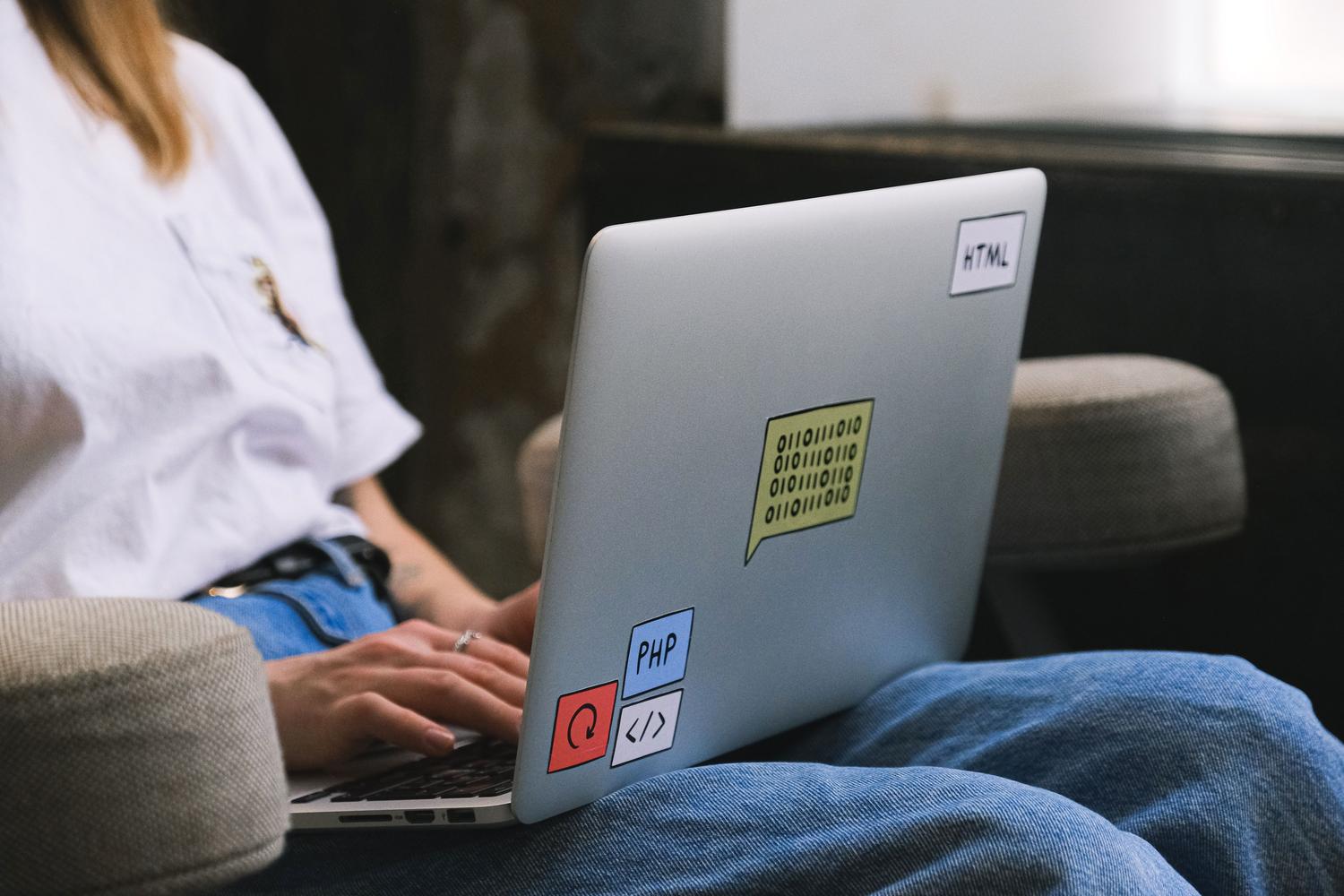 Persona programando en un portátil decorado con stickers de lenguajes de programación, representando el entorno de trabajo moderno de un desarrollador.