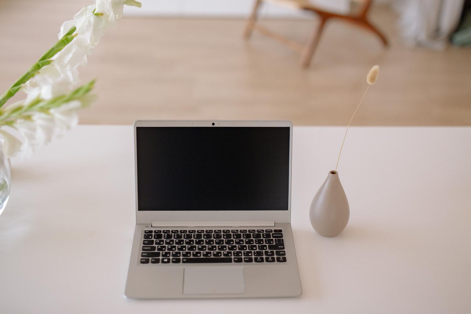 Espacio de trabajo minimalista con un portátil plateados y delgado sobre una mesa blanca, resaltando la estética limpia y moderna.
