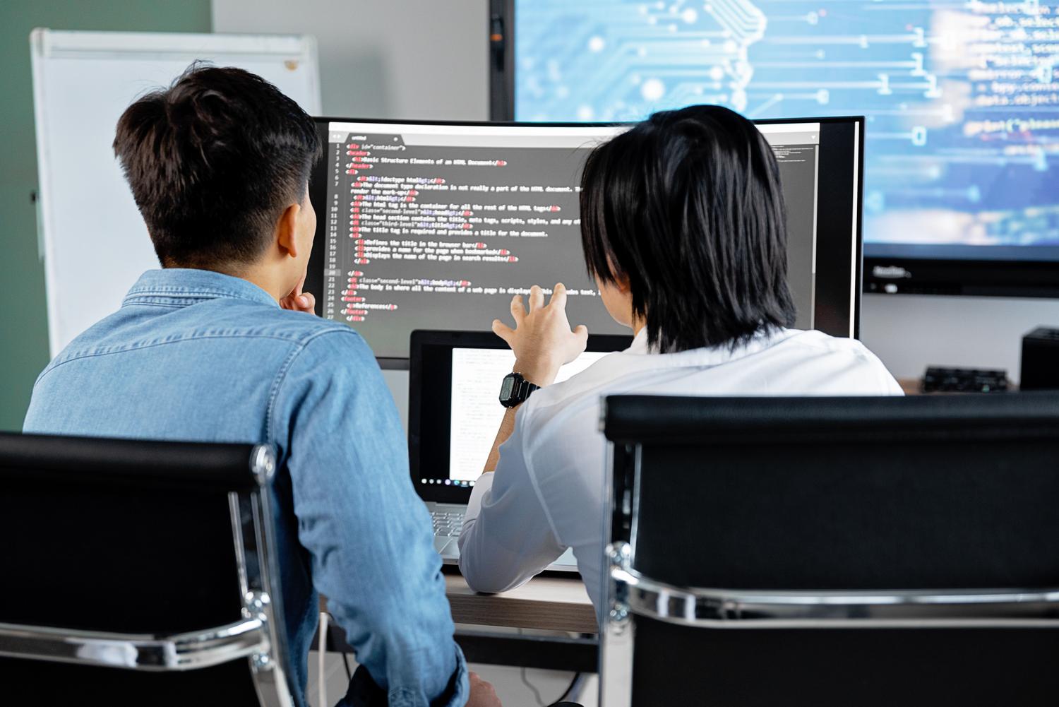Dos programadores revisando código juntos en un monitor, ilustrando el proceso de Pull Request y colaboración técnica.