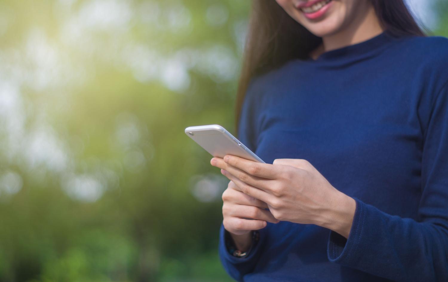 Mujer usando un smartphone en un entorno natural, representando la confianza y modernidad del usuario real en Facebook.