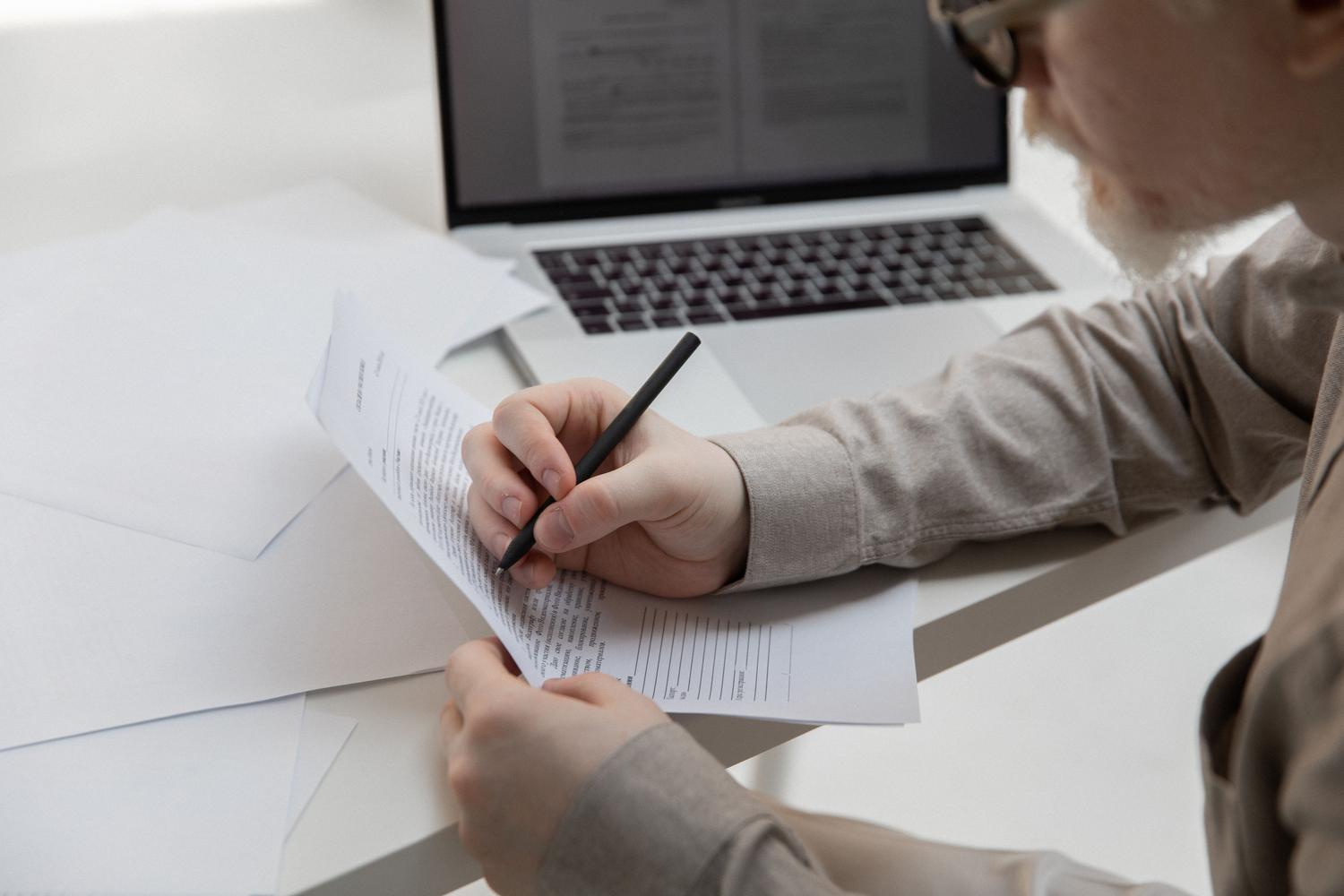 Primer plano de una persona revisando un documento impreso con un portátil al fondo, simbolizando la curación humana de textos generados por IA.