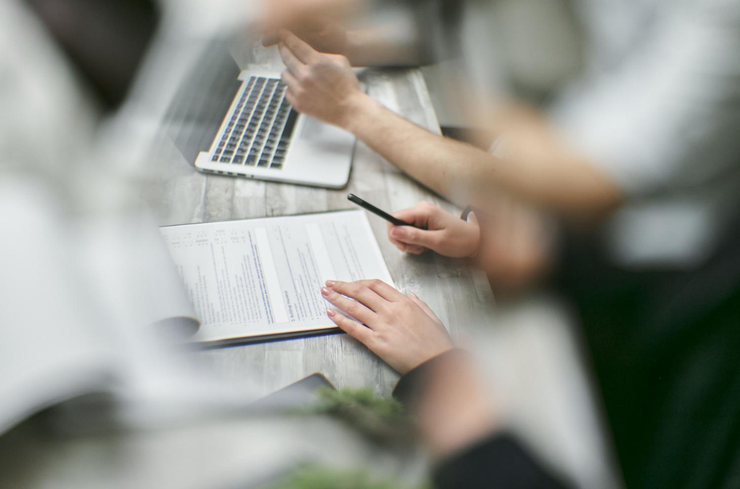 Profesionales colaborando en la redacción de documentos utilizando un ordenador portátil y papel.