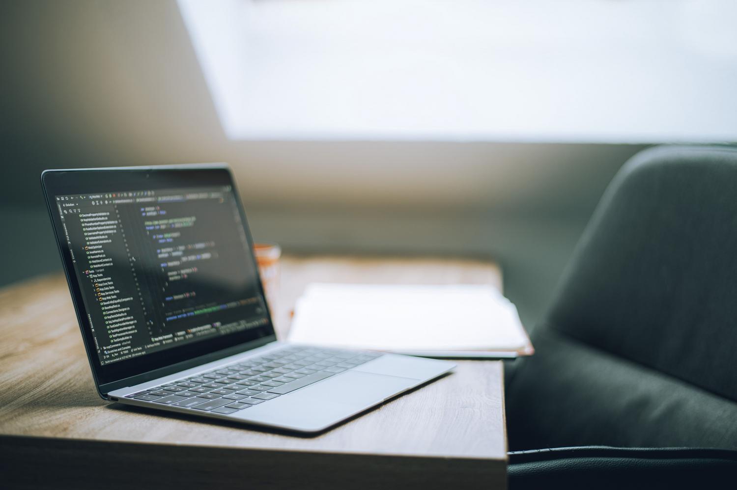Portátil abierto mostrando código de programación en un escritorio de oficina luminoso