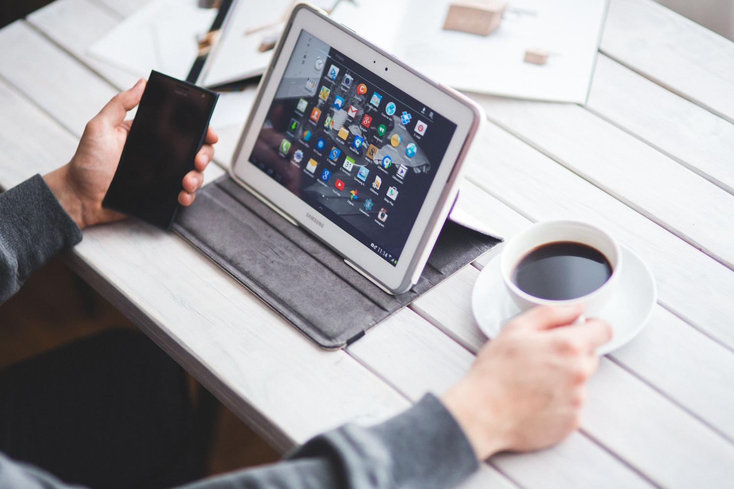 Persona utilizando simultáneamente una tablet y un smartphone, representando la sincronización de archivos en el ecosistema de Apple.