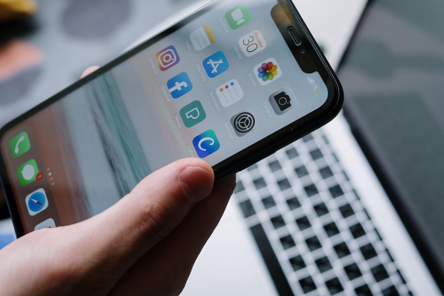 Persona sosteniendo un smartphone con iconos de aplicaciones y un portátil al fondo, representando la migración de datos y apps a la nube.