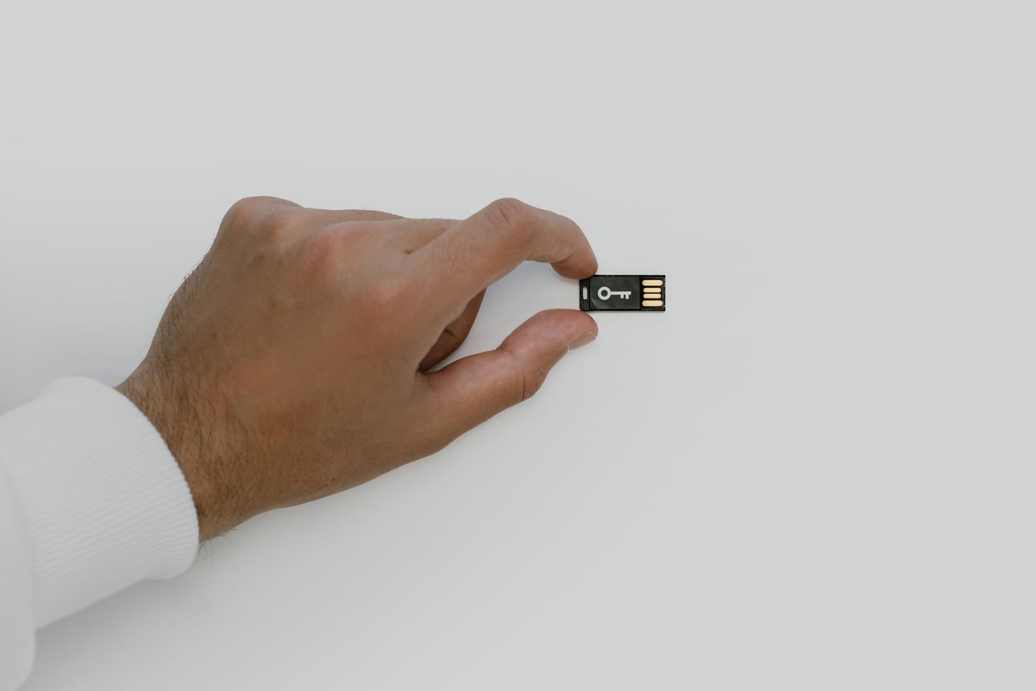 Mano sosteniendo un pendrive con el símbolo de una llave, representando el cifrado y la seguridad de los datos.
