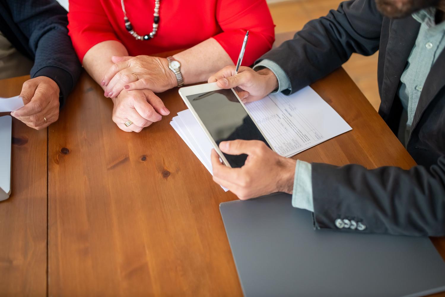 Reunión de negocios donde un consultor revisa y valida documentos en una tablet con sus colegas.