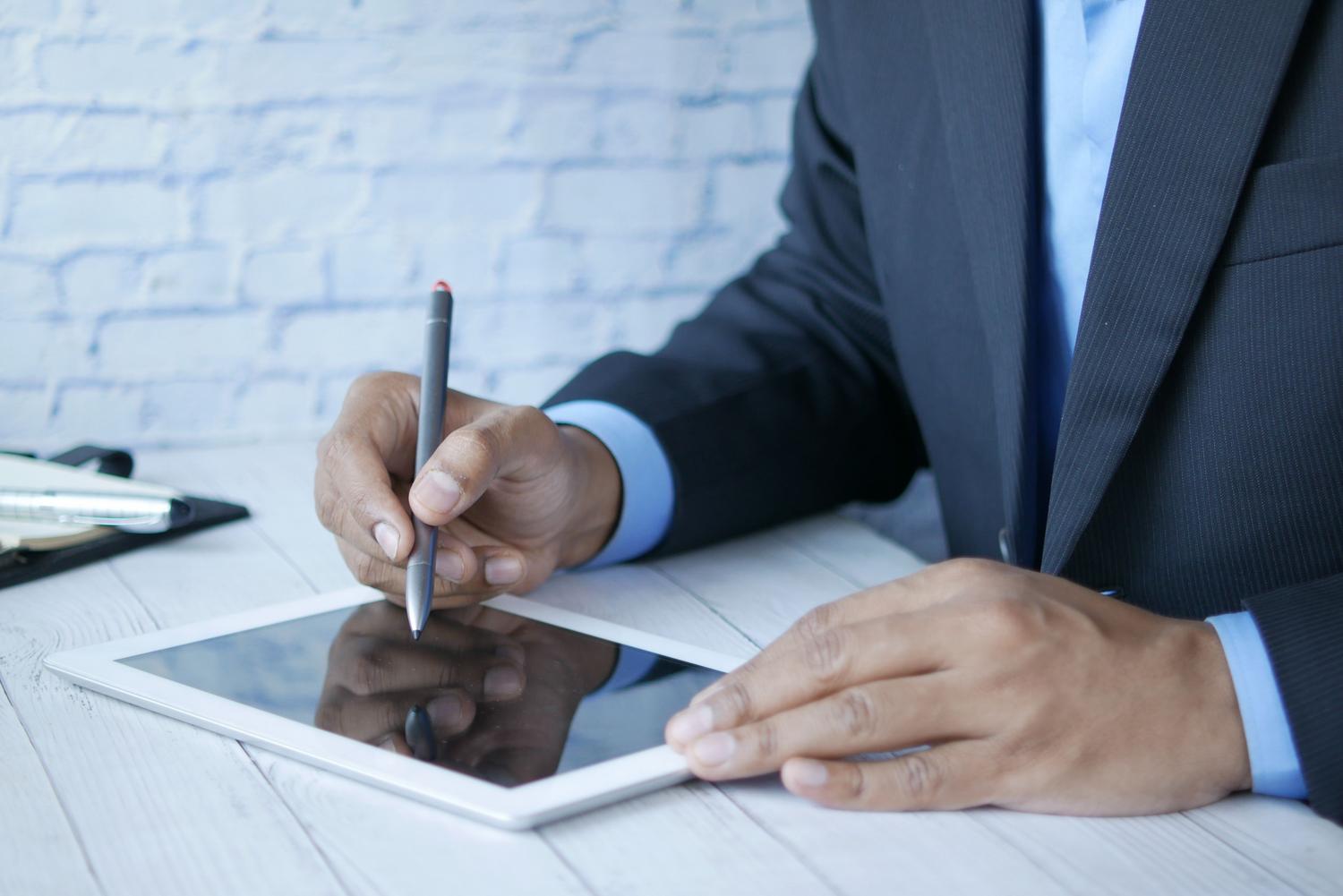 Primer plano de un profesional utilizando un lápiz digital para firmar un documento electrónico en una tablet.