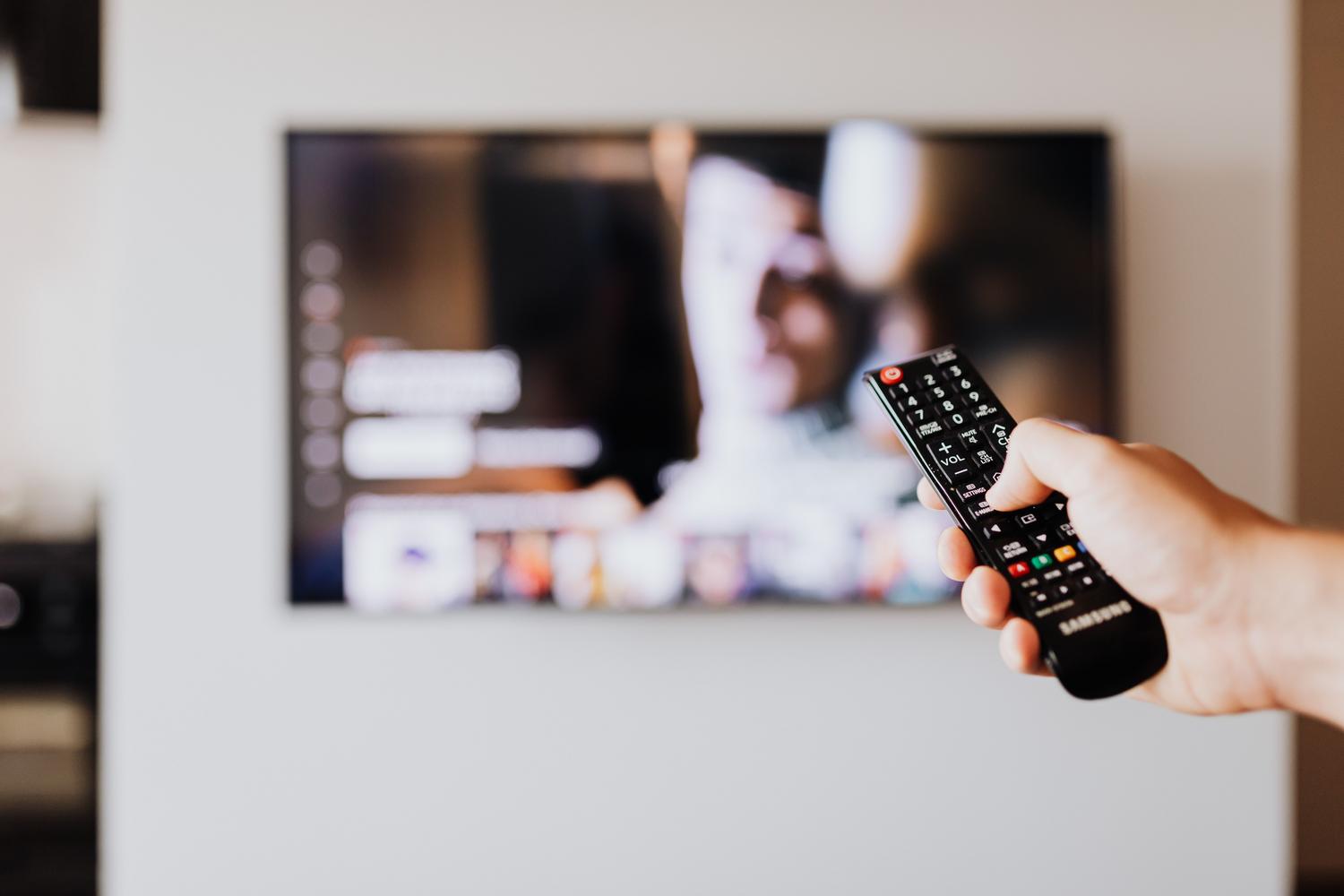 Primer plano de una mano utilizando el mando a distancia de un televisor para acceder al menú de ajustes.