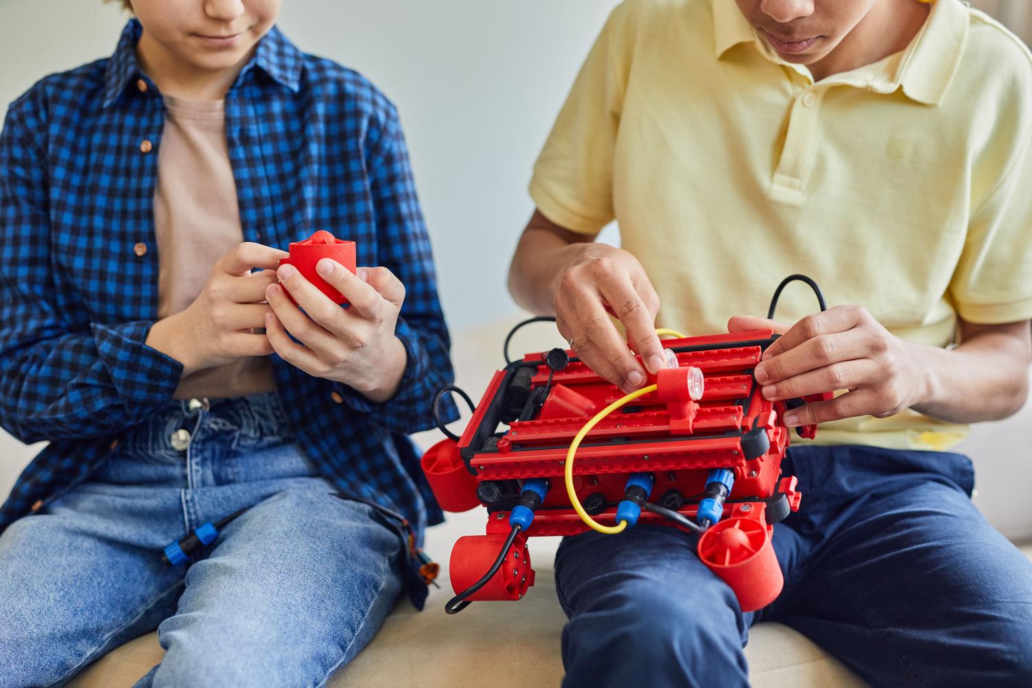 Plano detalle de las manos de dos niños ensamblando un robot, destacando la parte práctica de la ingeniería y el STEM.