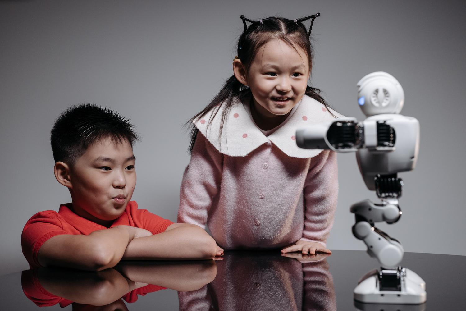Dos niños interactuando con un robot humanoide educativo en un aula, mostrando curiosidad y aprendizaje tecnológico.