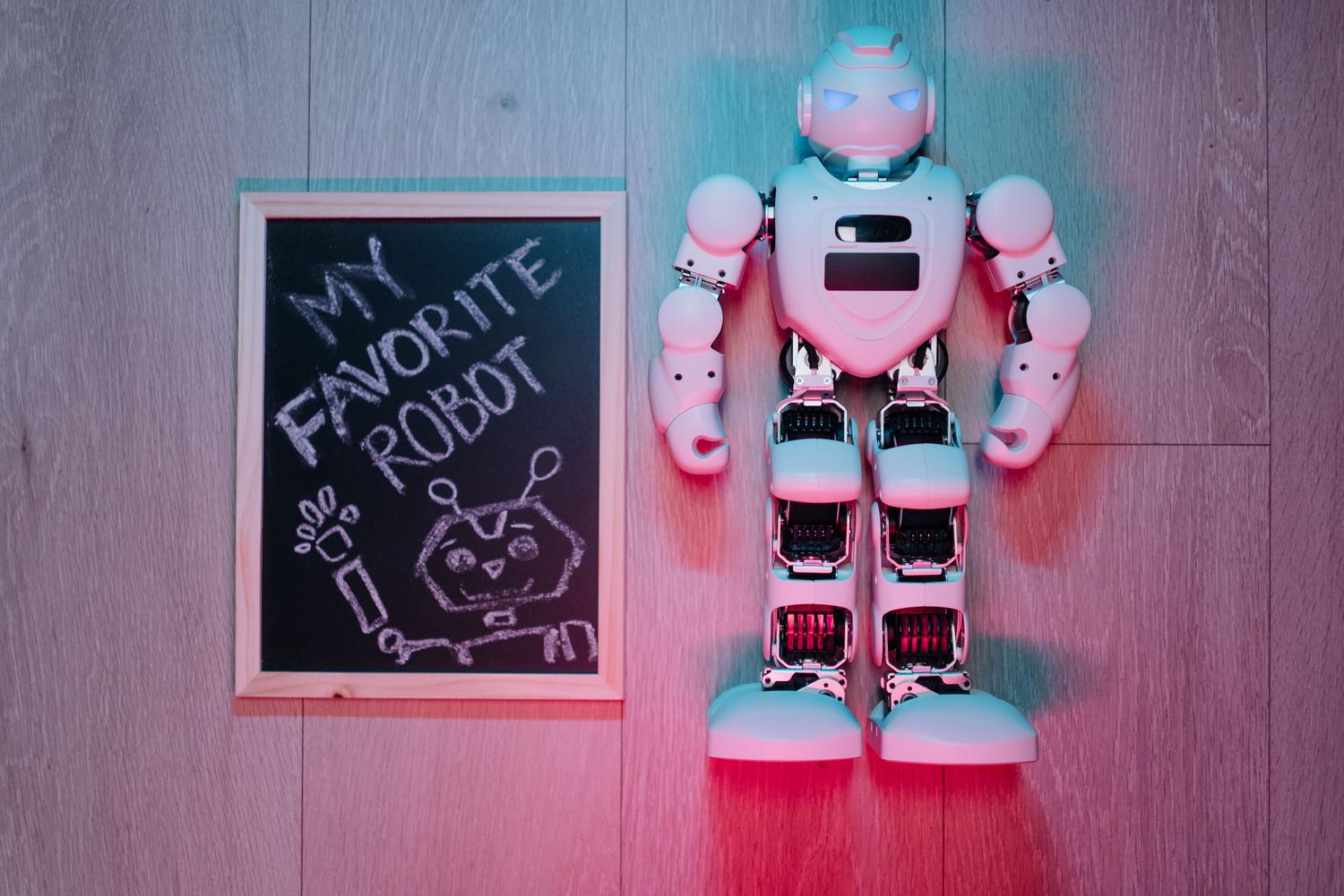 Comparación entre un dibujo infantil de un robot en una pizarra y un robot humanoide real, ilustrando la robótica teórica frente a la práctica.