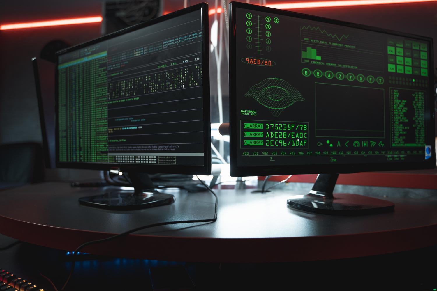 Configuración de doble monitor mostrando interfaces de programación y seguridad en una habitación oscura.