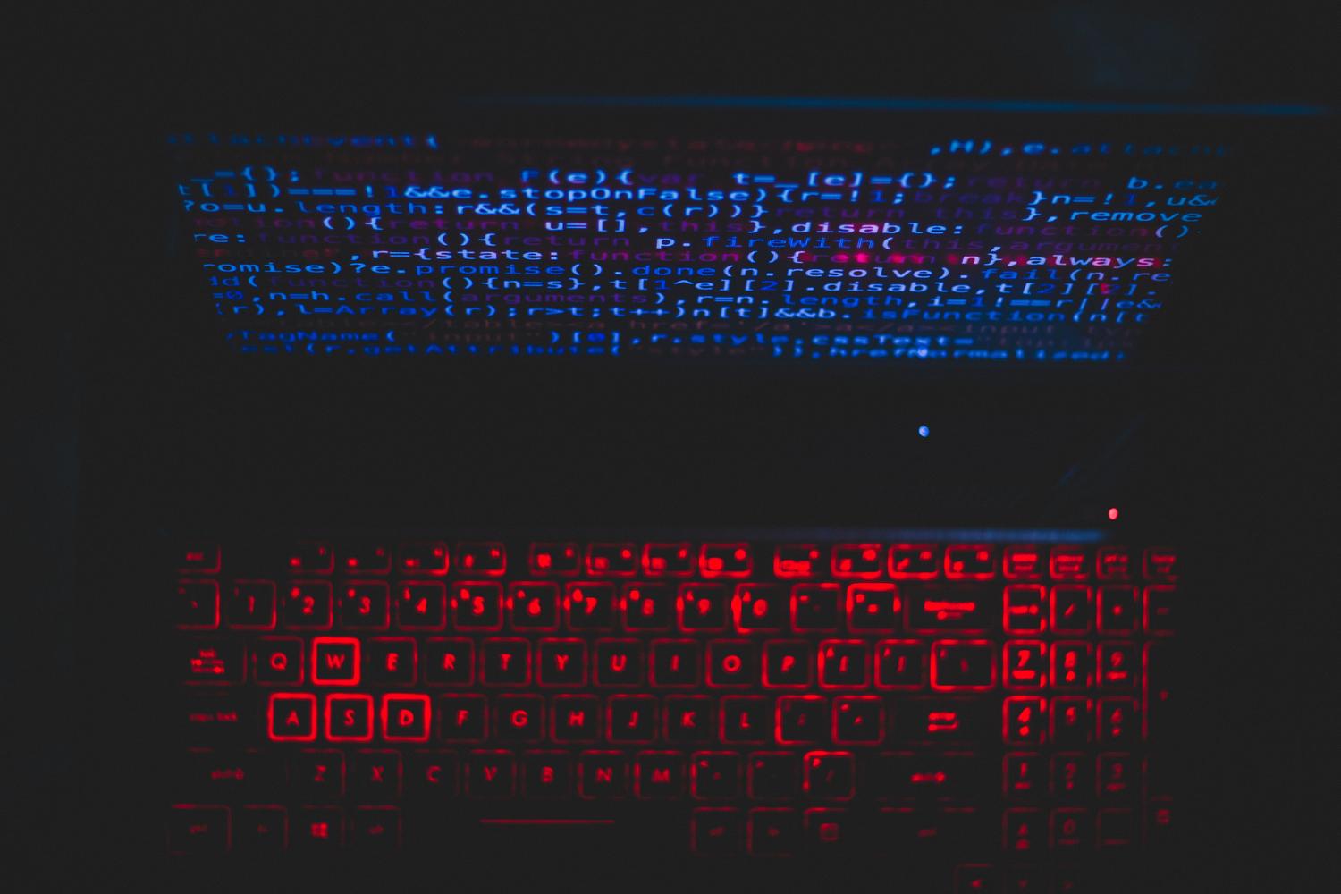 Configuración de portátil en entorno oscuro con teclado rojo brillante y código en pantalla, representando un entorno de ejecución de malware.