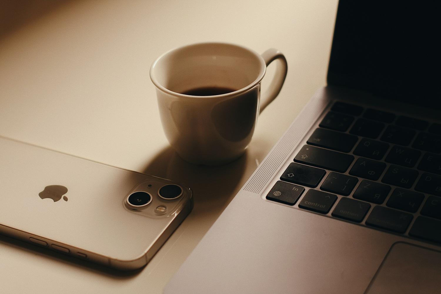Espacio de trabajo moderno con un smartphone, un ordenador portátil y una taza de café, ideal para ilustrar la productividad diaria.