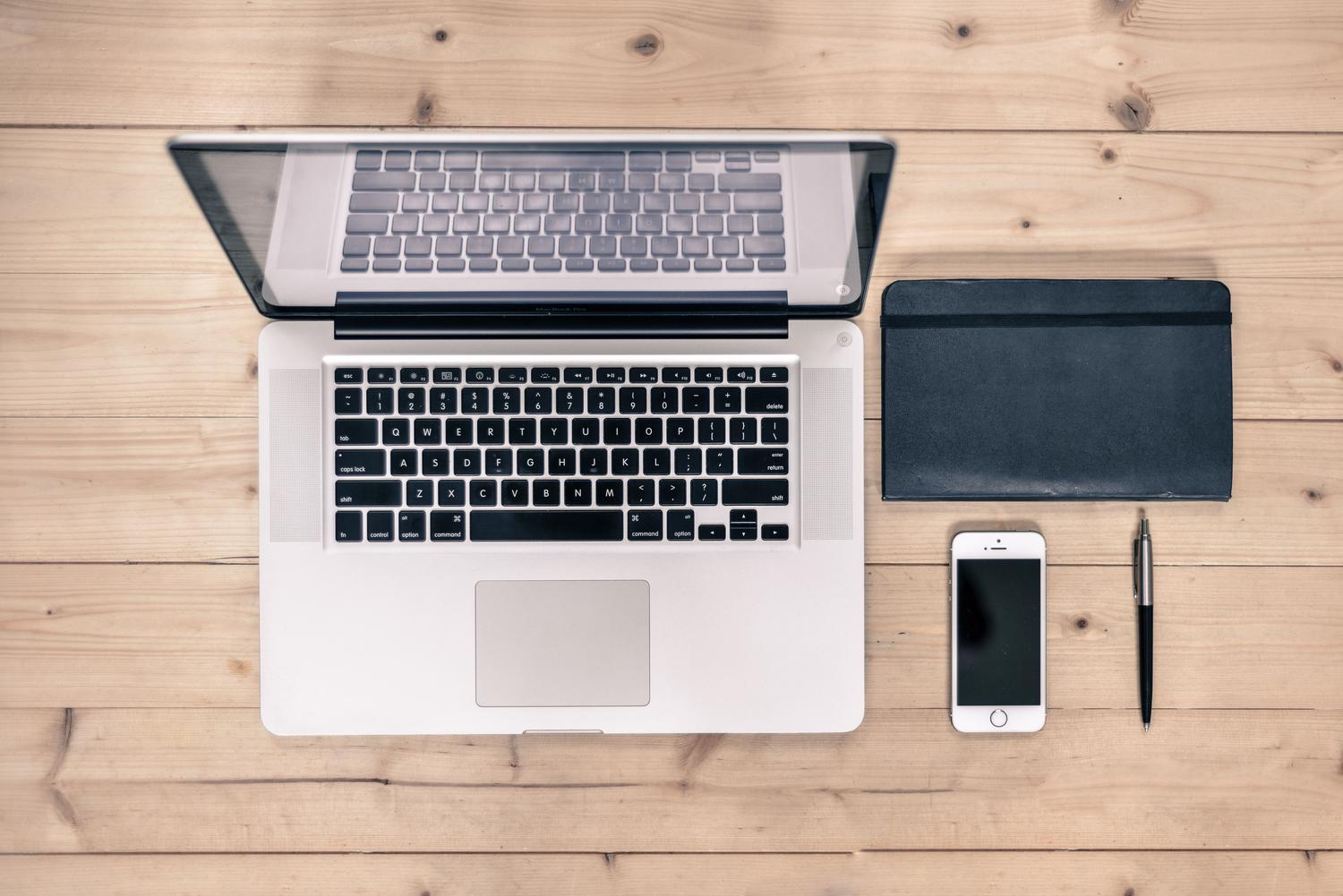 Vista cenital de un escritorio organizado con portátil, smartphone, libreta y bolígrafo, representando la configuración de trabajo.