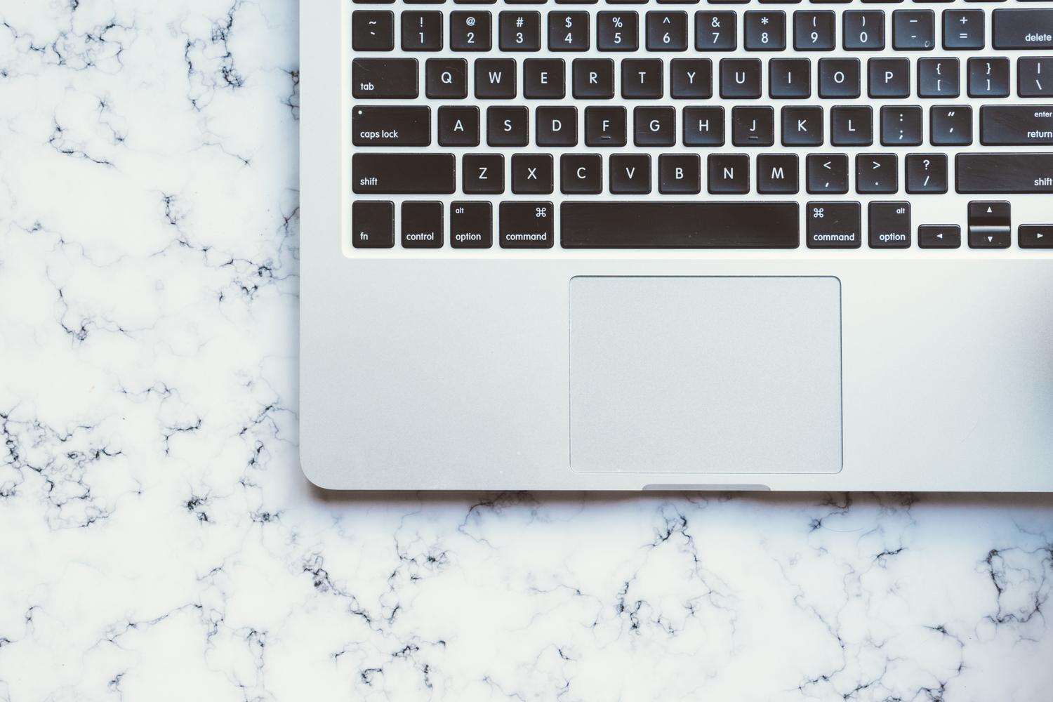 Vista cenital minimalista de un MacBook Pro sobre una superficie de mármol blanco, ideal como imagen de cabecera para un artículo técnico.
